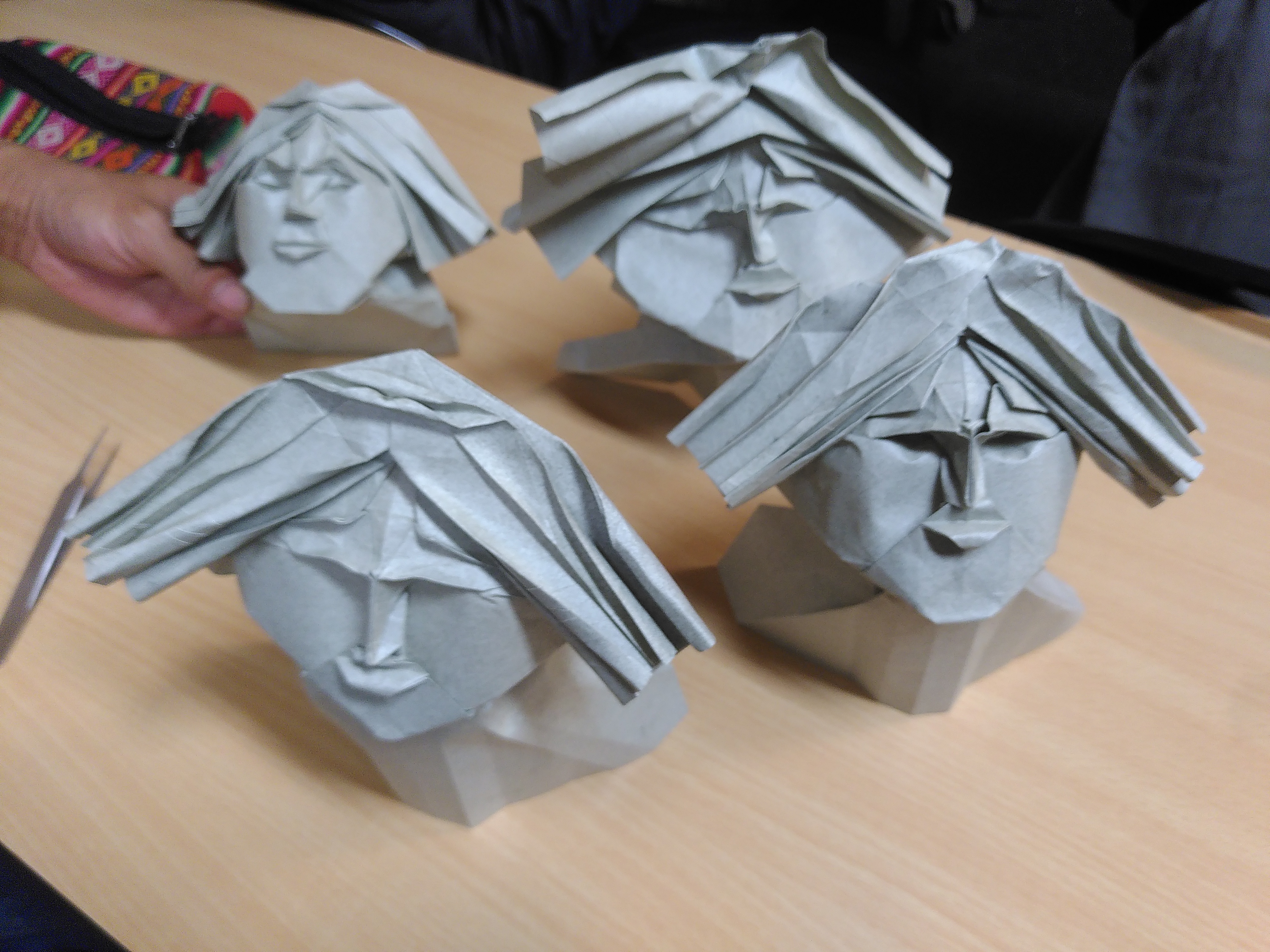 Quatre masques en origami, en papier peau d'éléphant. Ce sont des visages avec sourcils, bouche, nez, cheveux, menton, en relief, qui font un peu penser à des sculptures.