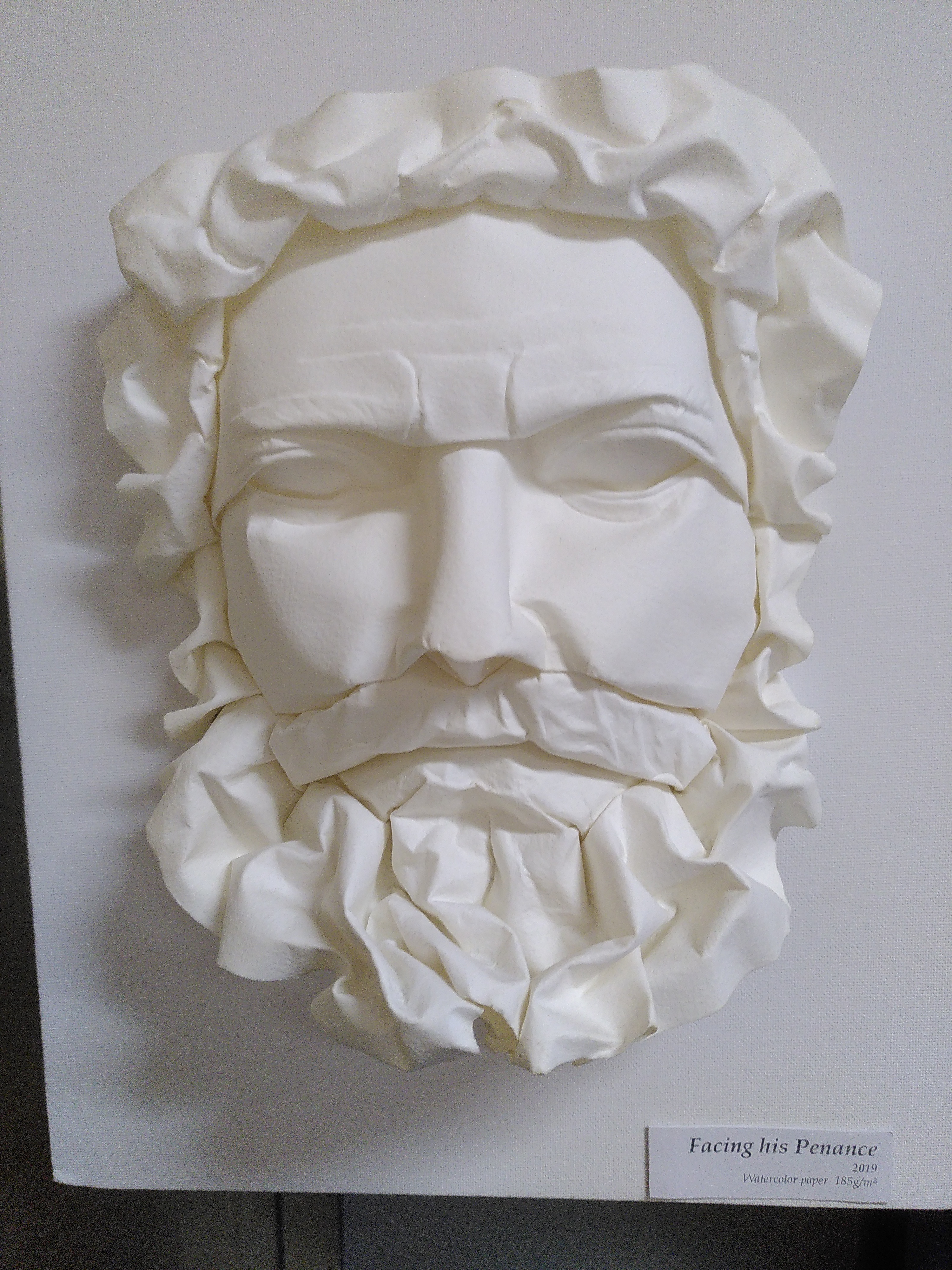 Un visage d'un homme barbu, chevelu et moustachu, d'un certain âge, qui a un visage sévère, réalisé en wet folding. L'œuvre porte le nom *Facing his penance*.