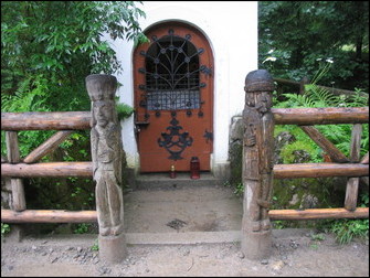Deux sculptures en bois, un montagnarde en costume folklorique et un mineur gardent l’accès vers une chapelle. Cliquez pour plus de commentaires
