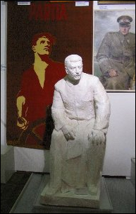 En arrière-plan, une tapisserie représentant le Parti comme un marin barrant un navire et un peinture représentant le maréchal Rokossovski. Au premier plan, statue de Staline. Le lien renvoie à la même photo agrandie, sans autre commentaire.
